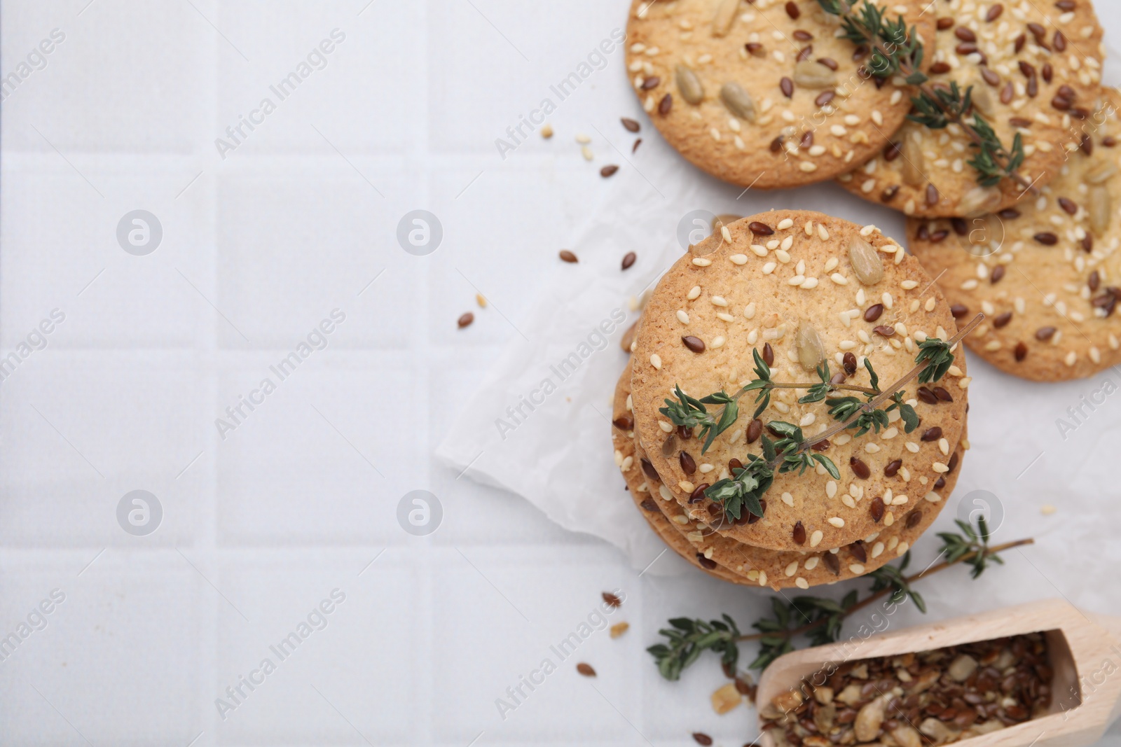 Photo of Cereal crackers with flax, sesame seeds and thyme on white tiled table, top view. Space for text