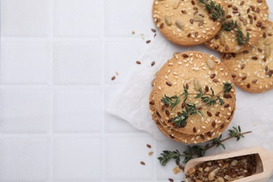 Photo of Cereal crackers with flax, sesame seeds and thyme on white tiled table, top view. Space for text