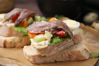Photo of Delicious bruschettas with anchovies, eggs, cream cheese, tomatoes, bell peppers and cucumbers on parchment, closeup