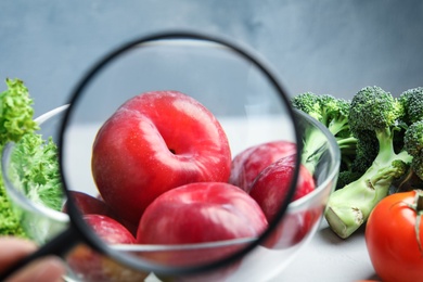 Photo of View through magnifying glass on plums, closeup. Poison detection