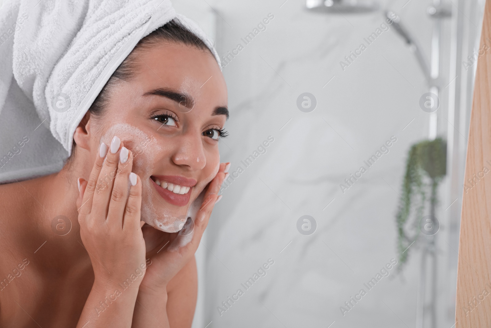 Photo of Beautiful young woman applying cleansing foam onto face in bathroom, space for text. Skin care cosmetic