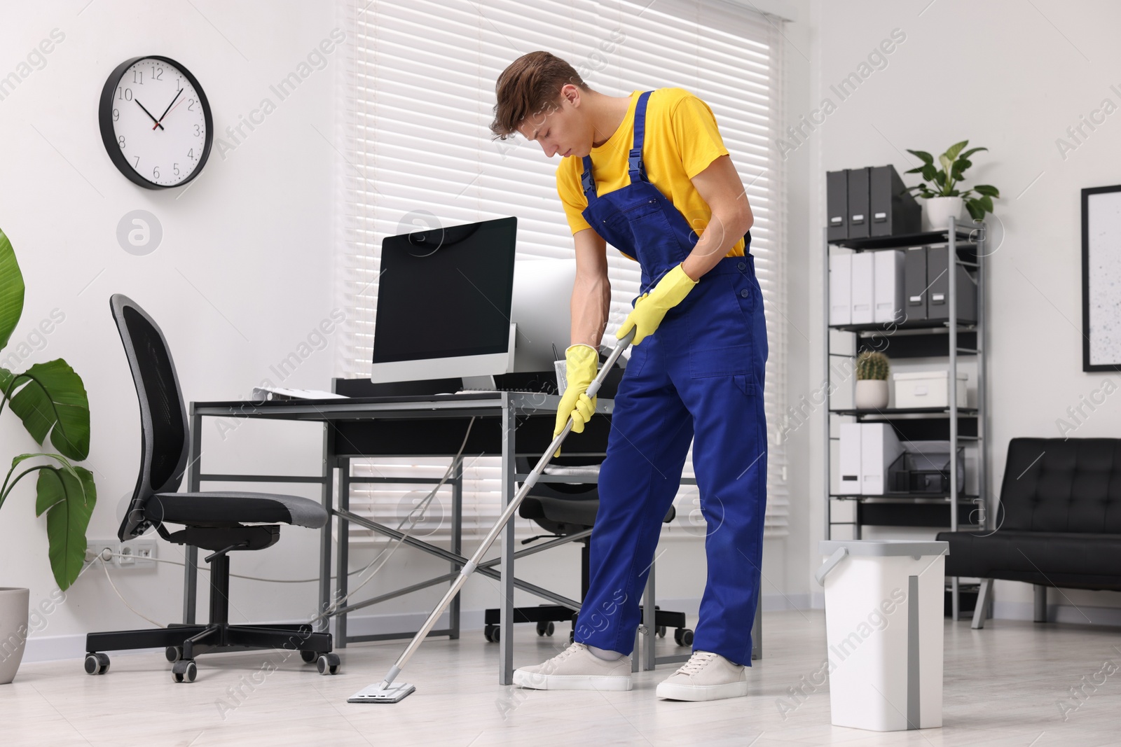 Photo of Cleaning service. Man washing floor with mop in office