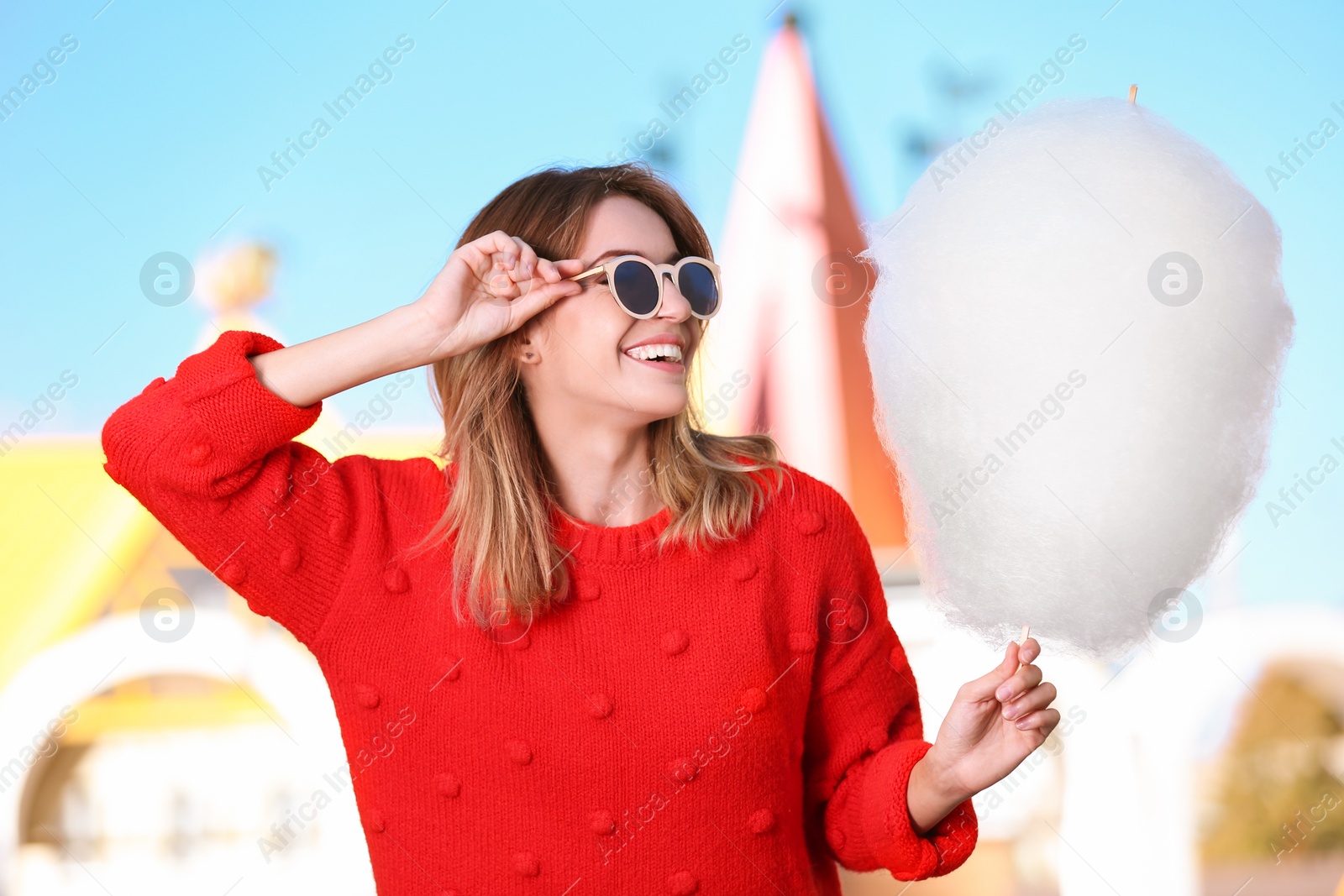 Photo of Young cheerful woman having fun with  cotton candy in amusement park