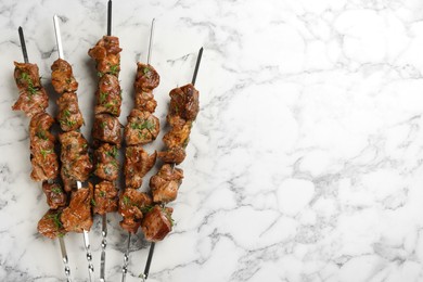 Photo of Metal skewers with delicious meat on white marble table, flat lay. Space for text