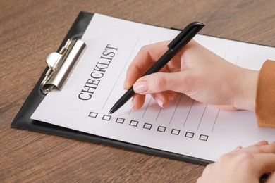 Photo of Woman filling Checklist at wooden table, closeup