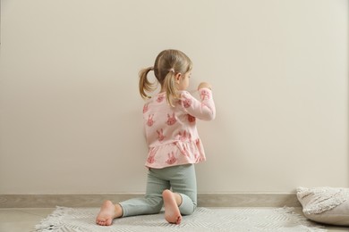 Little girl drawing on beige wall indoors, back view. Child`s art