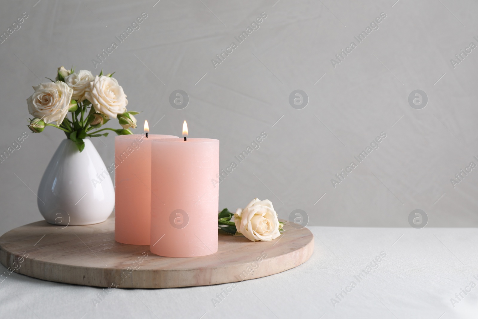 Photo of Burning candles and beautiful roses on white table, space for text