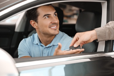 Photo of Young salesman giving car key to customer in modern auto dealership, closeup