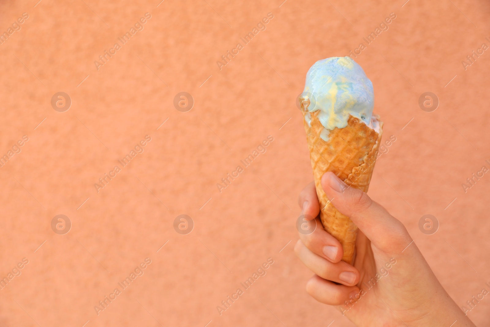 Photo of Woman holding delicious ice cream in wafer cone near coral wall outdoors, closeup. Space for text
