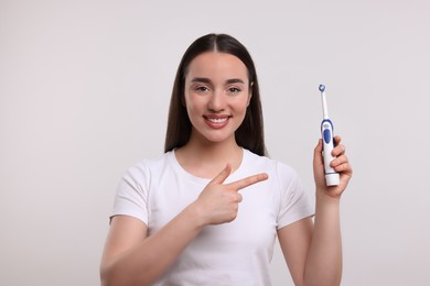 Photo of Happy young woman holding electric toothbrush on white background