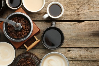 Different coffee drinks in cups, beans and manual grinder on wooden table, flat lay. Space for text