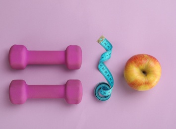 Photo of Fresh apple, measuring tape and dumbbells on color background, top view. Healthy diet