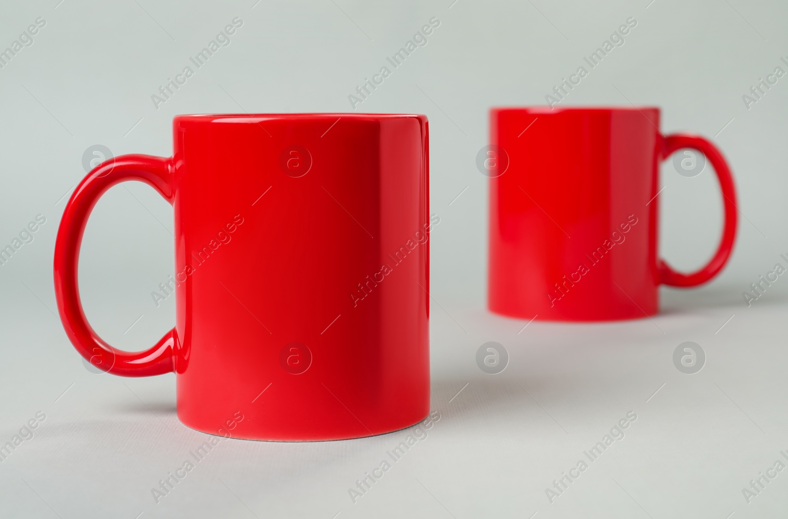 Photo of Two red ceramic mugs on light grey background