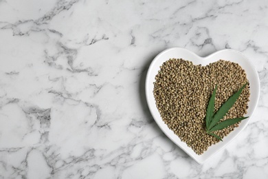 Photo of Plate with hemp seeds and space for text on marble background, top view