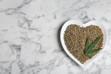 Plate with hemp seeds and space for text on marble background, top view