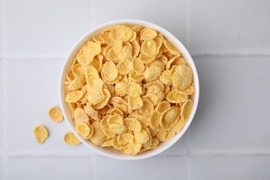 Tasty crispy corn flakes in bowl on white tiled table, top view. Breakfast cereal