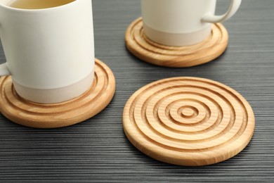 Stylish wooden cup coasters and mugs on black table