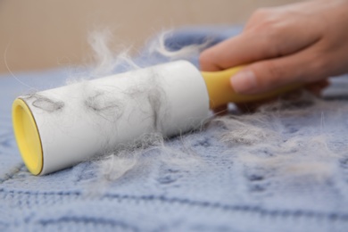 Photo of Woman removing hair from light blue knitted fabric with lint roller, closeup