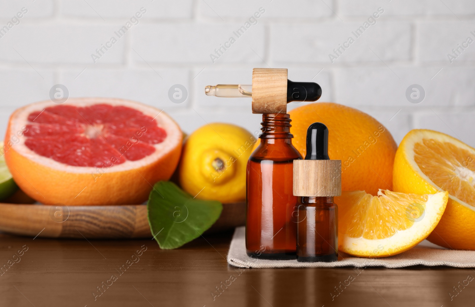 Photo of Bottles of essential oils with different citrus fruits and leaf on wooden table against white brick wall