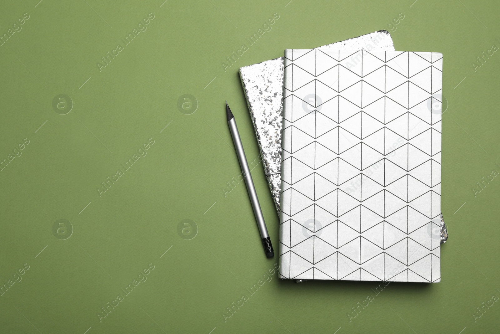 Photo of White notebooks and pencil on green background, flat lay. Space for text