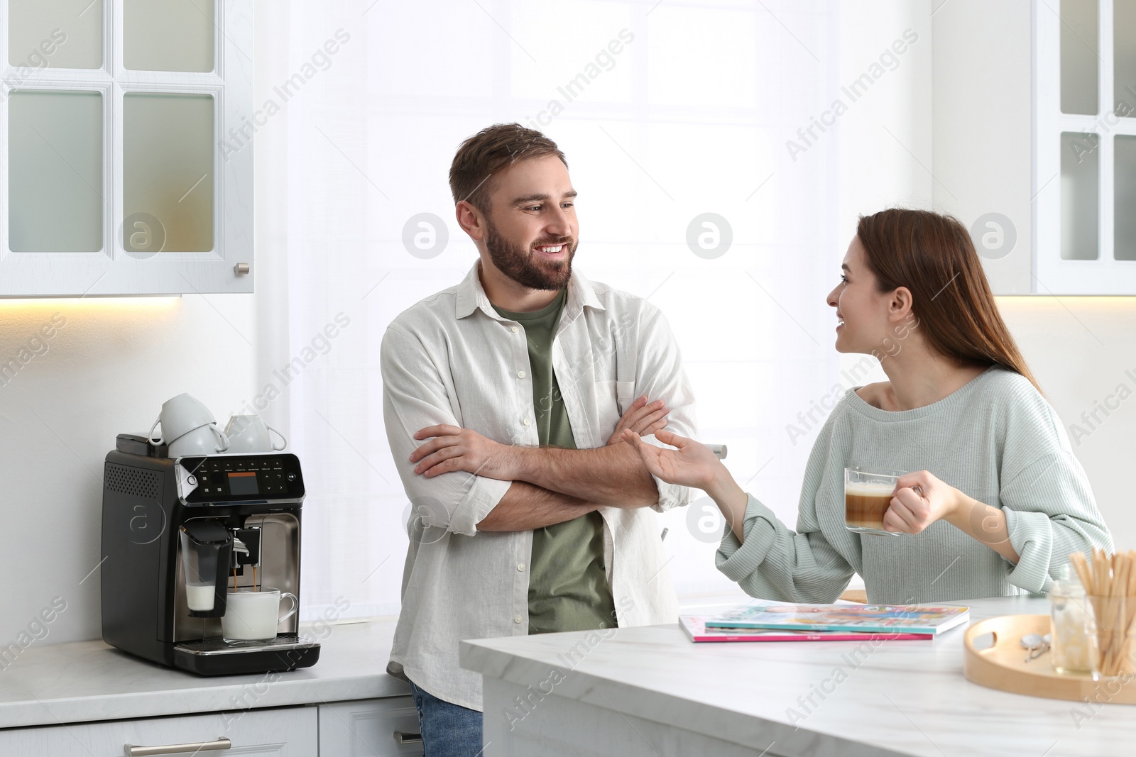 Photo of Young man talking with his girlfriend while using modern coffee machine in kitchen