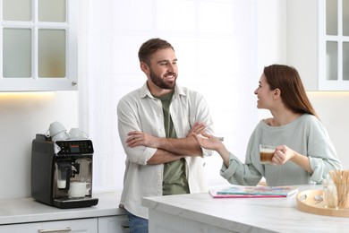 Young man talking with his girlfriend while using modern coffee machine in kitchen