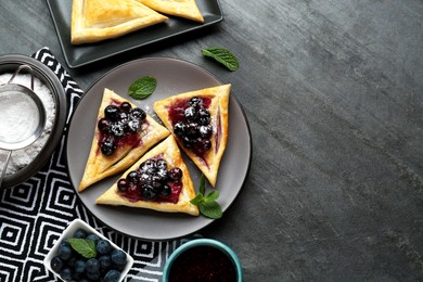 Fresh tasty puff pastry with sugar powder, jam, sweet berries and mint served on grey table, flat lay. Space for text
