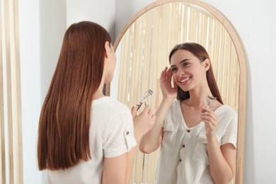 Photo of Woman with eyelash curler near mirror at home
