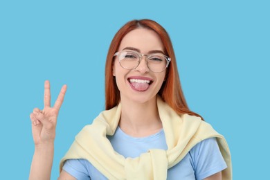 Photo of Happy woman showing her tongue and V-sign on light blue background