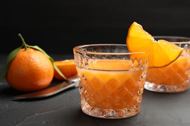 Photo of Tasty tangerine liqueur in glasses and fresh citrus fruits on black textured table, closeup