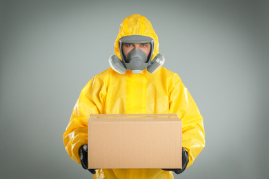 Man wearing chemical protective suit with cardboard box on light grey background. Prevention of virus spread