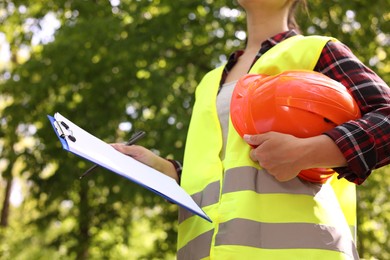 Forester with hard hat and clipboard examining plants in forest, closeup