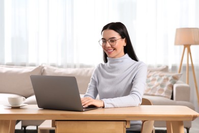 Happy woman working with laptop at wooden desk in room