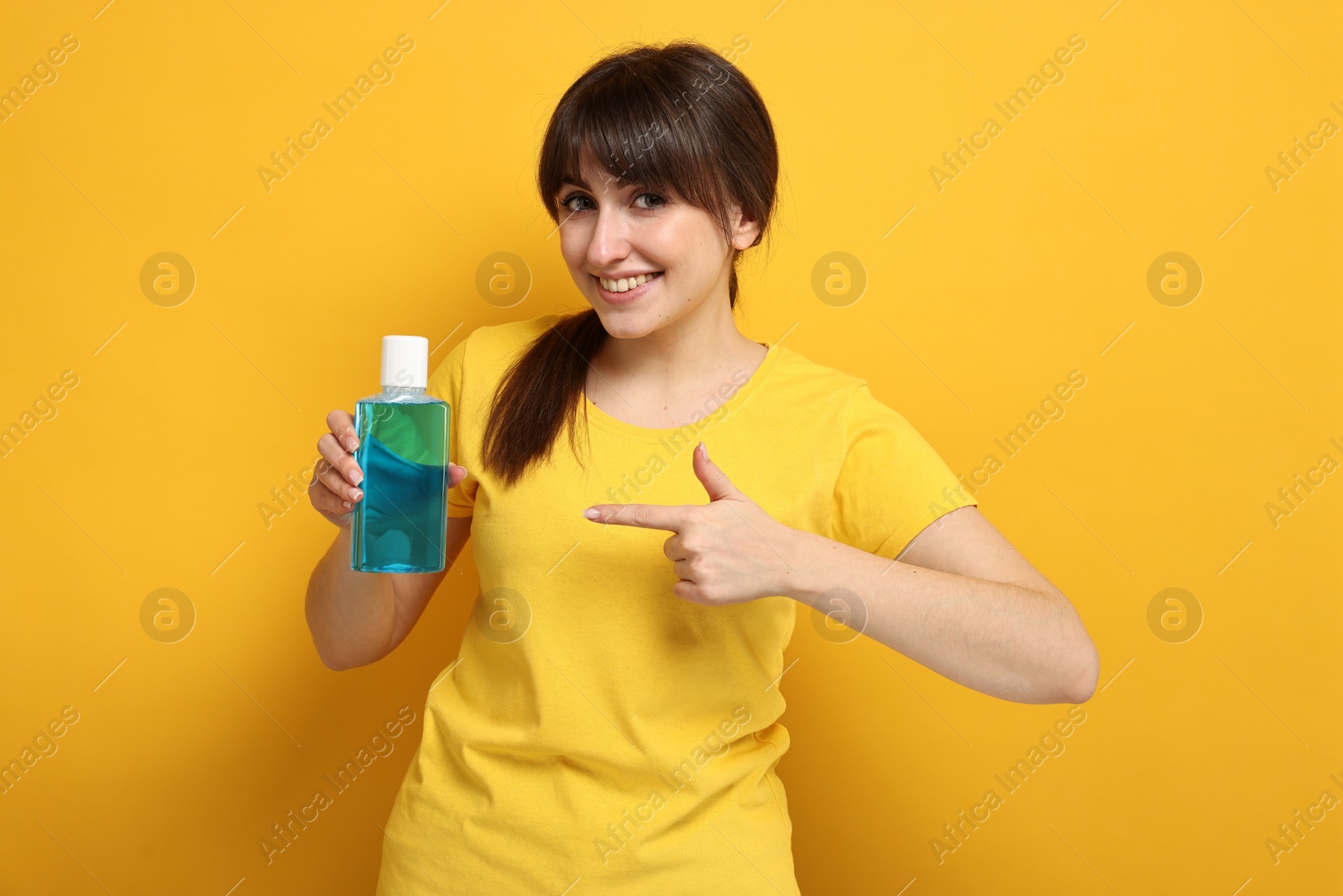 Photo of Young woman pointing at mouthwash on yellow background