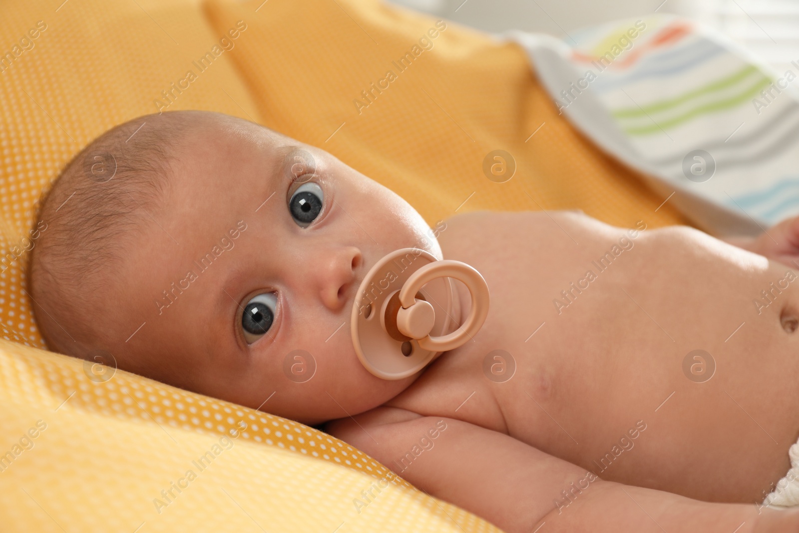 Photo of Cute little baby with pacifier lying on yellow plaid