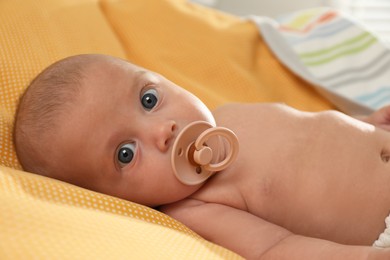 Photo of Cute little baby with pacifier lying on yellow plaid