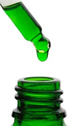 Photo of Dripping green facial serum from pipette into glass bottle on white background, closeup