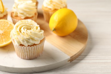 Tasty cupcakes with cream, zest and lemons on white wooden table, closeup. Space for text