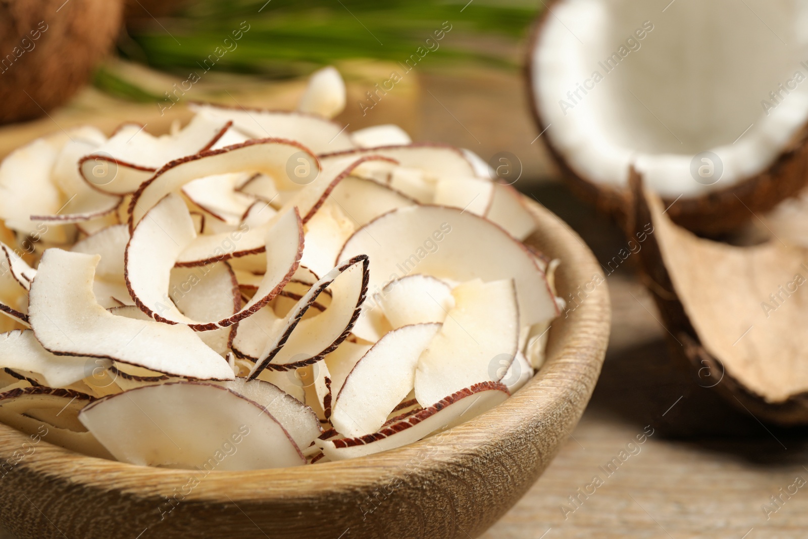 Photo of Tasty coconut chips in wooden bowl, closeup