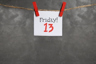 Photo of Paper note with phrase Friday! 13 hanging on twine against grey background, space for text. Bad luck superstition