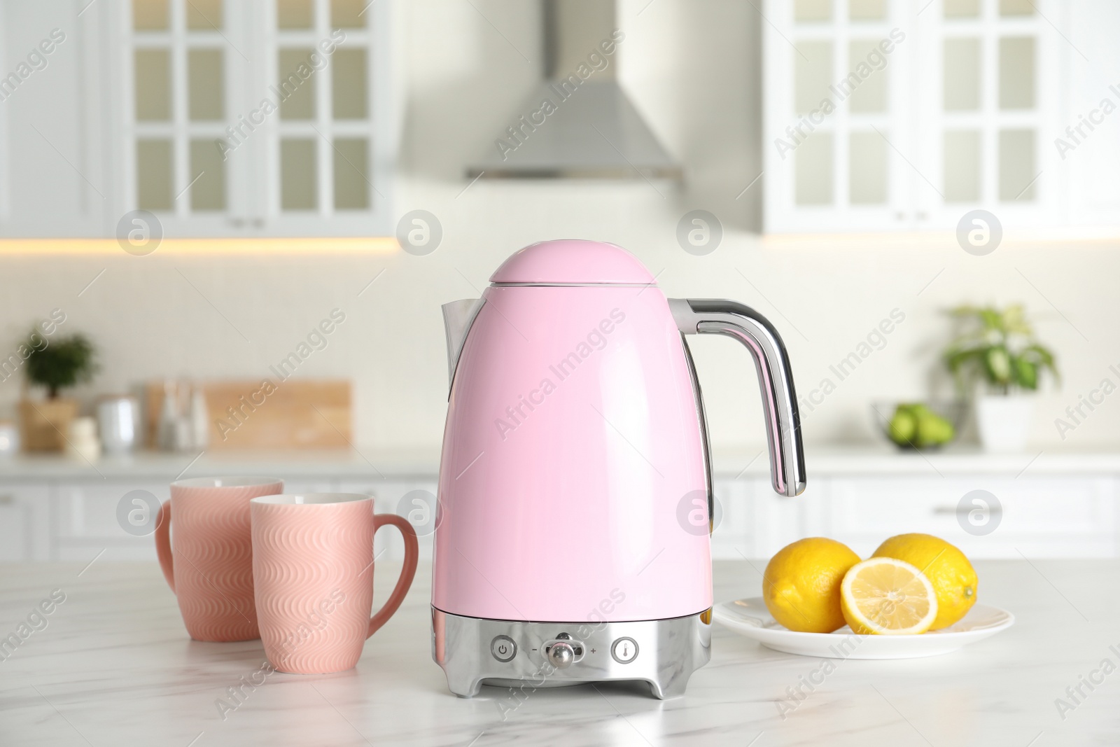 Photo of Modern electric kettle, cups and lemons on table in kitchen