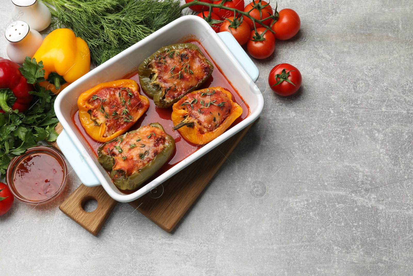 Photo of Tasty stuffed peppers in dish and ingredients on grey table, flat lay. Space for text