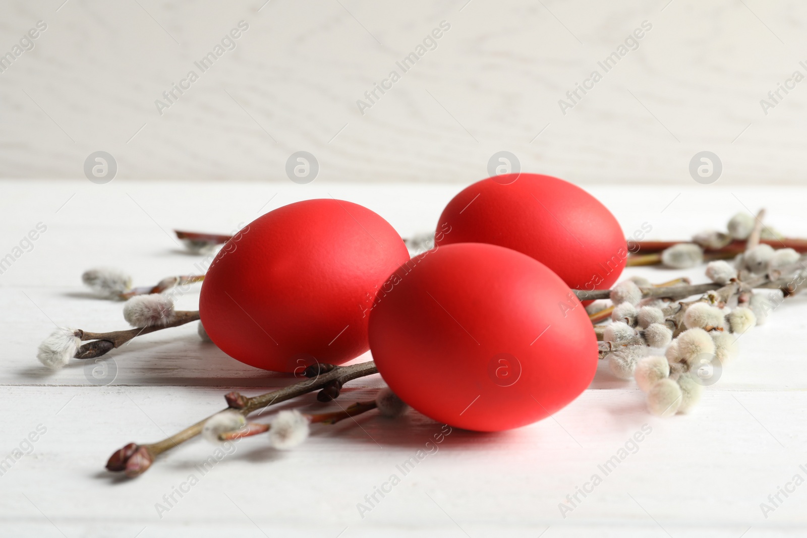 Photo of Red dyed Easter eggs and pussy willow on wooden table against light background