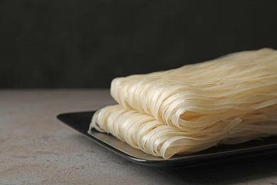 Plate with raw rice noodles on table, closeup. Space for text