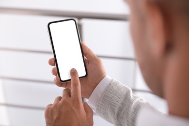 Man using mobile phone with empty screen indoors, closeup