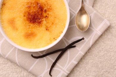 Photo of Delicious creme brulee in bowl, vanilla pods and spoon on light textured table, top view