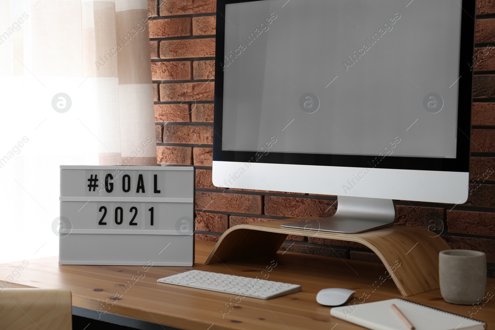 Photo of Light box with hashtag Goal 2021 near computer monitor on wooden desk in office