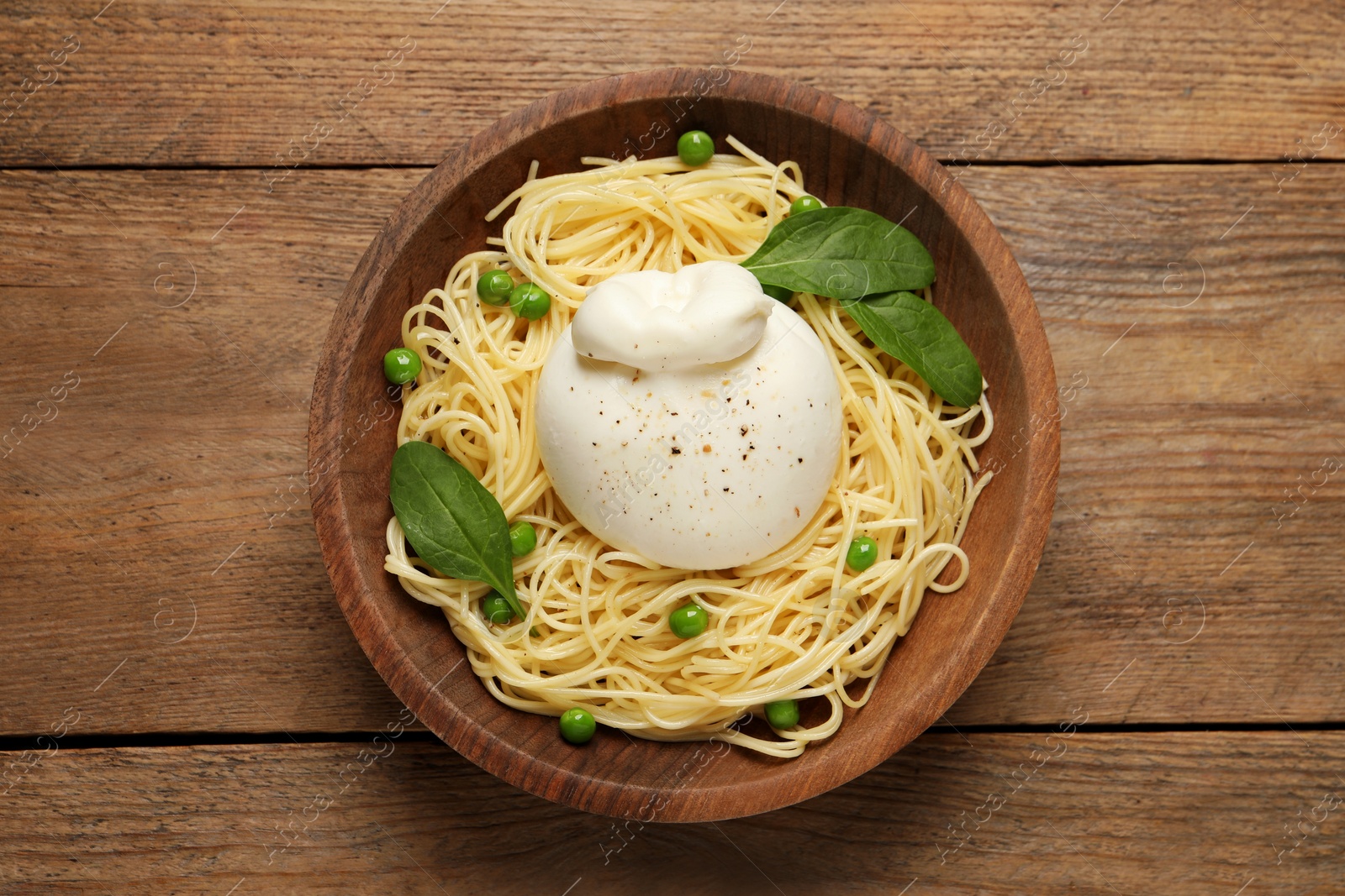 Photo of Bowl of delicious pasta with burrata, peas and spinach on wooden table, top view