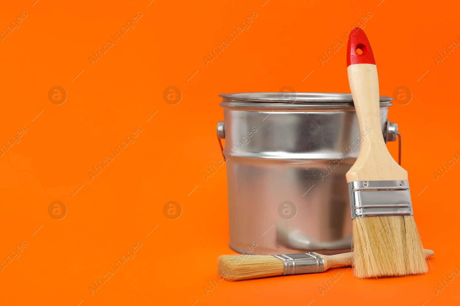 Photo of Can of orange paint and brushes on color background. Space for text