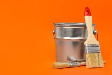 Photo of Can of orange paint and brushes on color background. Space for text